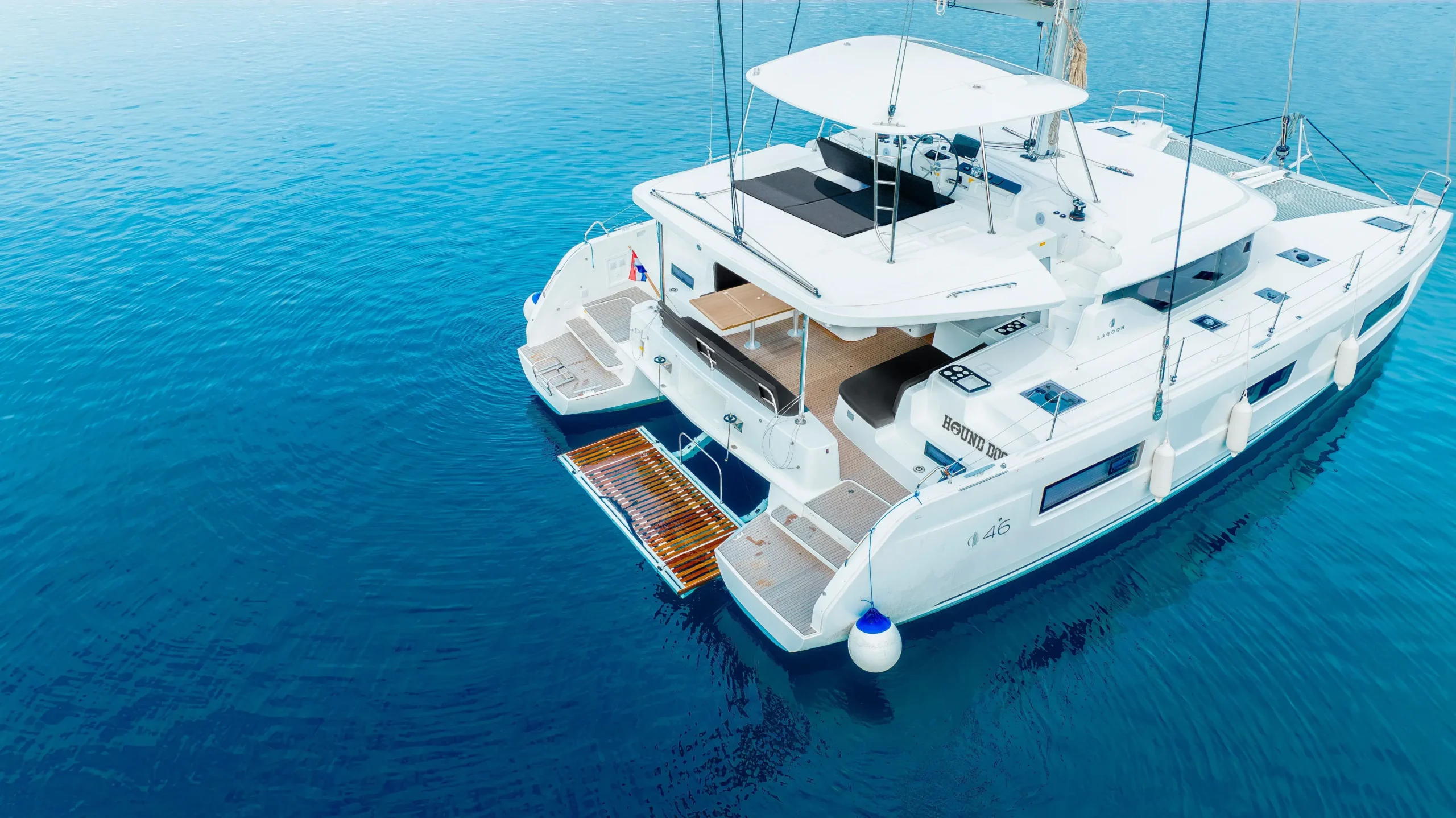 Aerial view of a white luxury catamaran yacht anchored on calm blue ocean water.