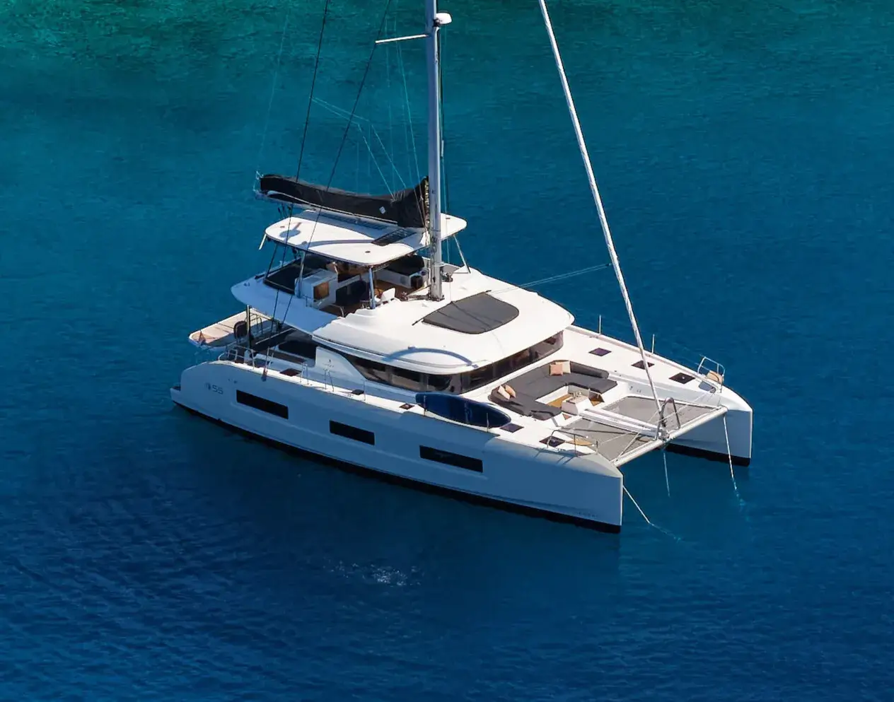 White catamaran sailing yacht anchored on calm blue sea, with shaded cockpit and sun loungers.
