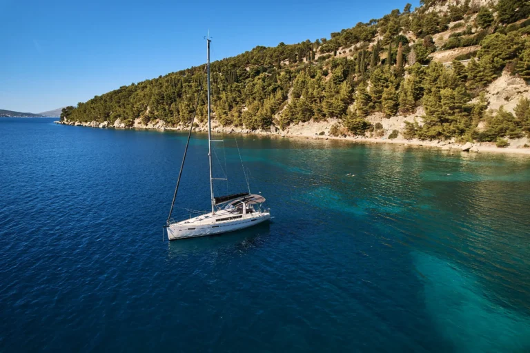 Sailboat anchored in calm blue sea beside a rocky, forested shoreline