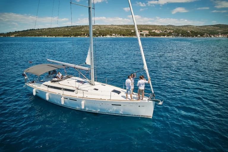 White catamaran sailing on blue water with four people on deck and a coastal town in the distance