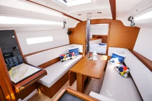 Cozy sailboat cabin with white cushions, colorful pillows, wooden table, and skylight overhead.