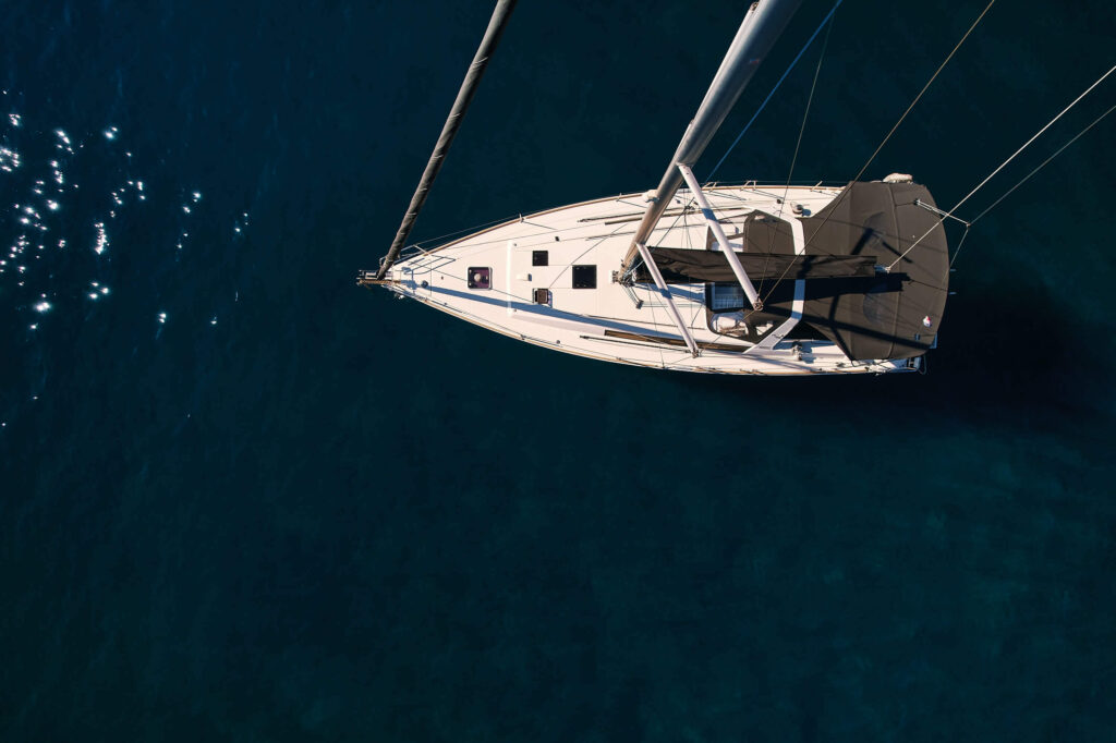 Top-down aerial view of a white sailboat sailing on dark blue water with its rigging visible