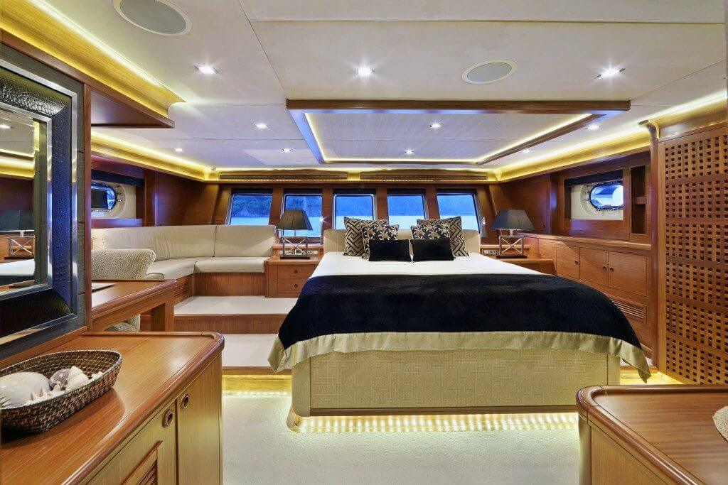Luxurious yacht bedroom with a king bed, beige bedding, and warm wood paneling in a spacious cabin.