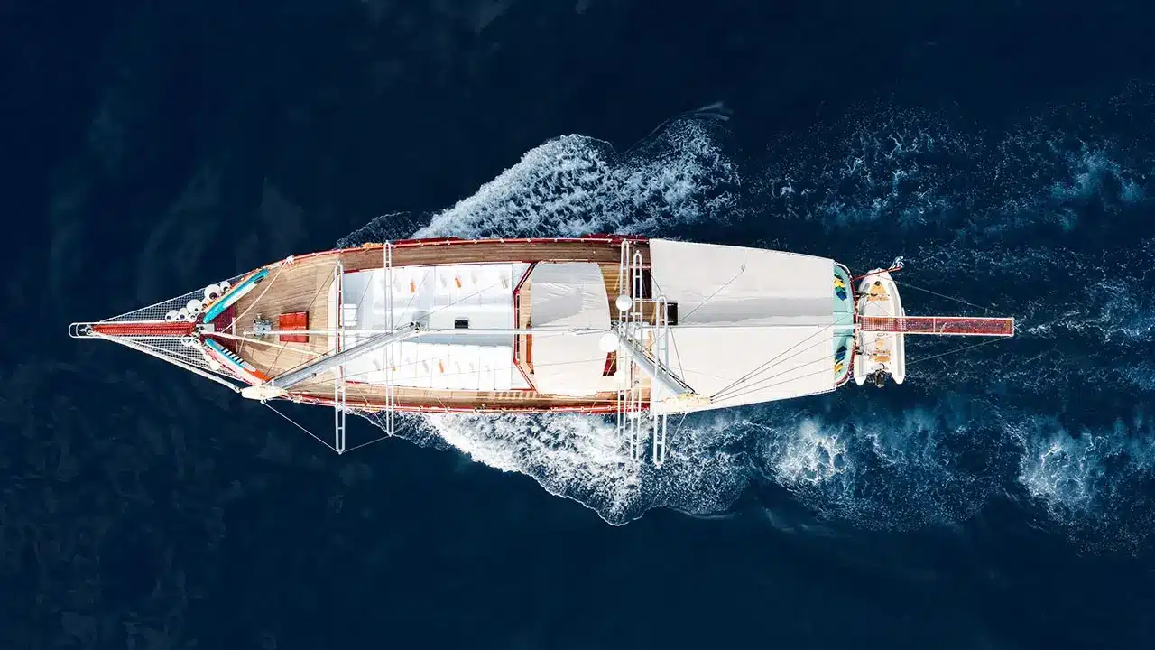 Top-down aerial view of a wooden sailing yacht cruising through dark blue ocean.