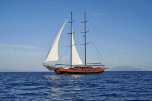 Two-masted wooden sailing ship with white sails gliding on a calm blue sea under a clear sky