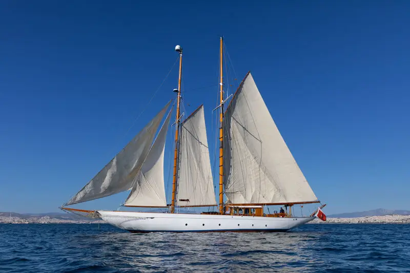 Two-masted sailing schooner with white sails gliding on blue water near a distant coastline