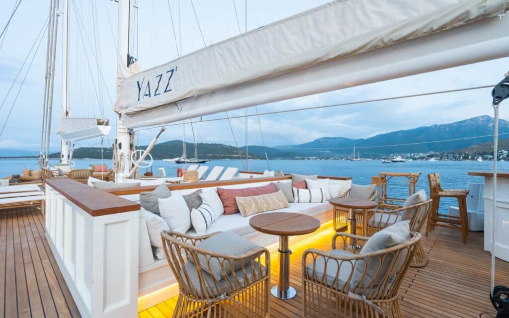Luxurious white yacht deck with beige cushioned seating, wooden tables, and blue water in the background.