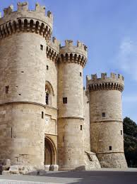 exp-rhode-3 | Sail in Greece™ Stone medieval castle with three cylindrical towers and a central arched entrance under a blue sky.