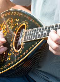 exp-rhode-4 | Sail in Greece™ Close-up of a person’s hands playing a decorated mandolin with intricate inlay on a dark body.