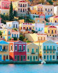 exp-rhode-5 | Sail in Greece™ Colorful row houses along a harbor in a seaside village with water in the foreground.