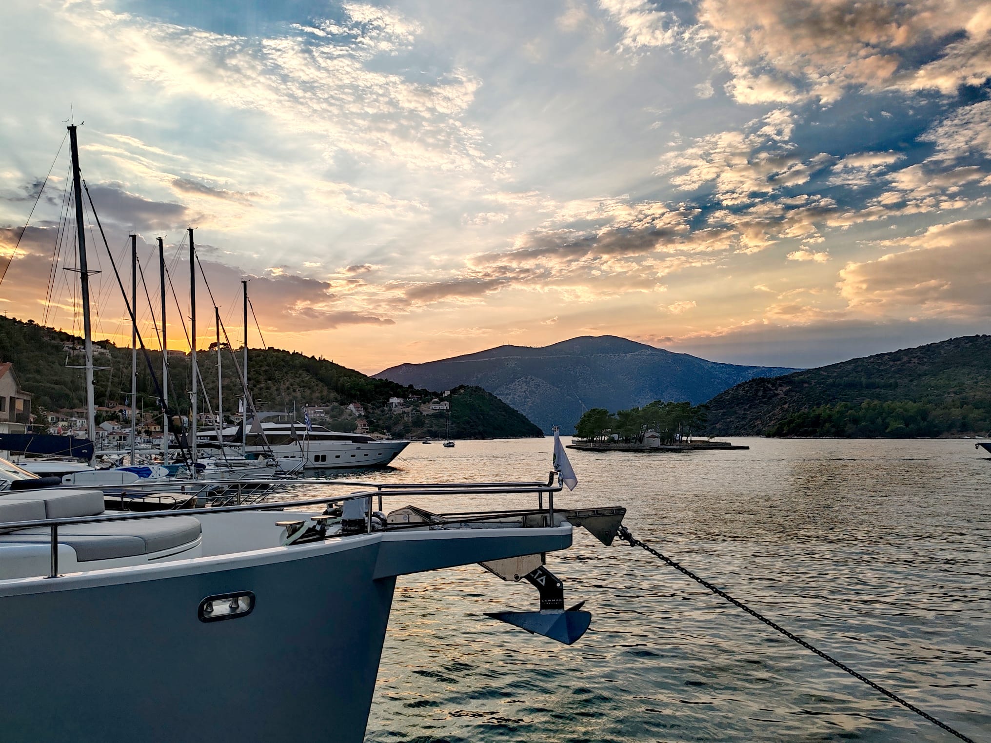 Boats docked at a marina with a sunset sky and hills in the background.